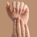 Hands of a beautiful well-groomed woman with feminine nails on a beige background. Manicure, pedicure beauty salon concept. Empty space for text or logo. On nails nude gel polish. High quality photo